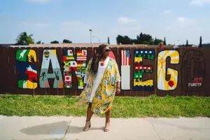 bagLady Meredith SanDiego in front of wooden fence painted with a sign Sandiego